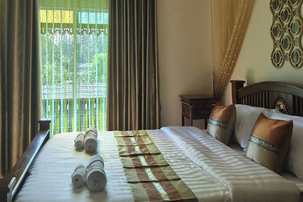A hotel room with a bed, a window with curtains, an air conditioning unit, and a decorative mirror on the wall.