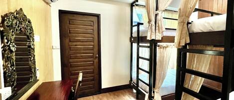 Una habitación con literas, una puerta de madera, un espejo y una ventana con cortinas.