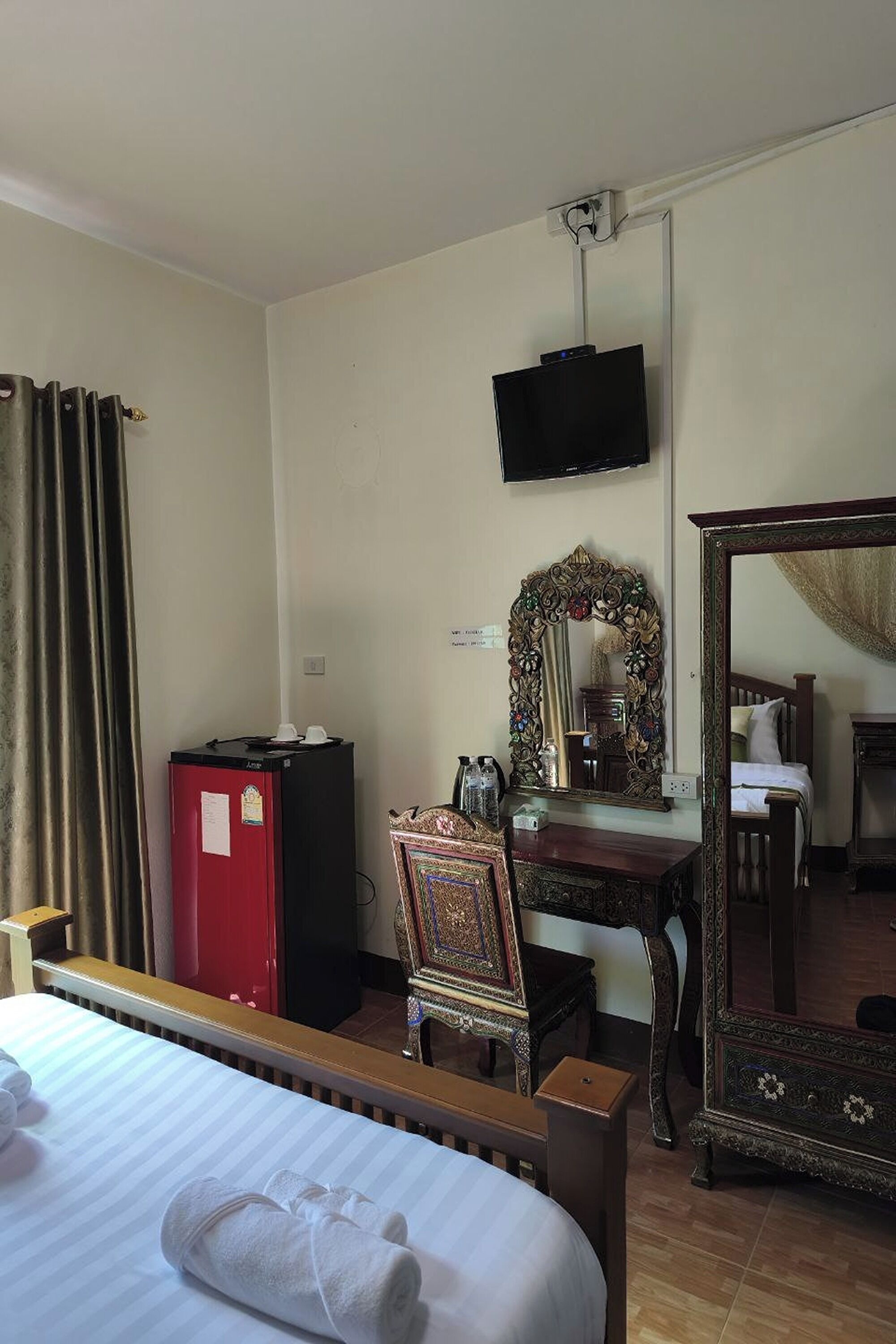 A hotel room with a bed, a desk with a mirror, a television mounted on the wall, and a wardrobe.