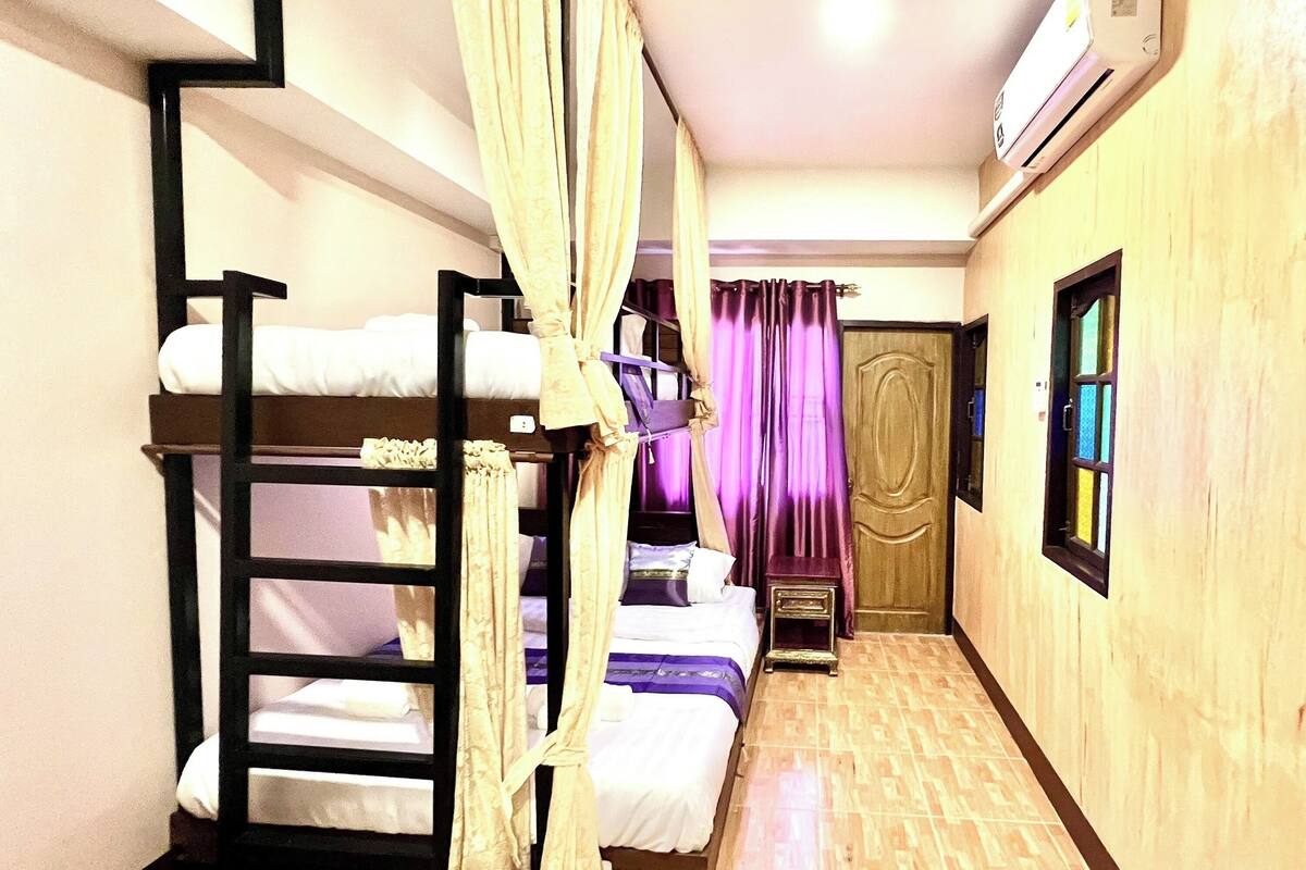 A room with bunk beds, a wooden floor, a door, and an air conditioning unit.