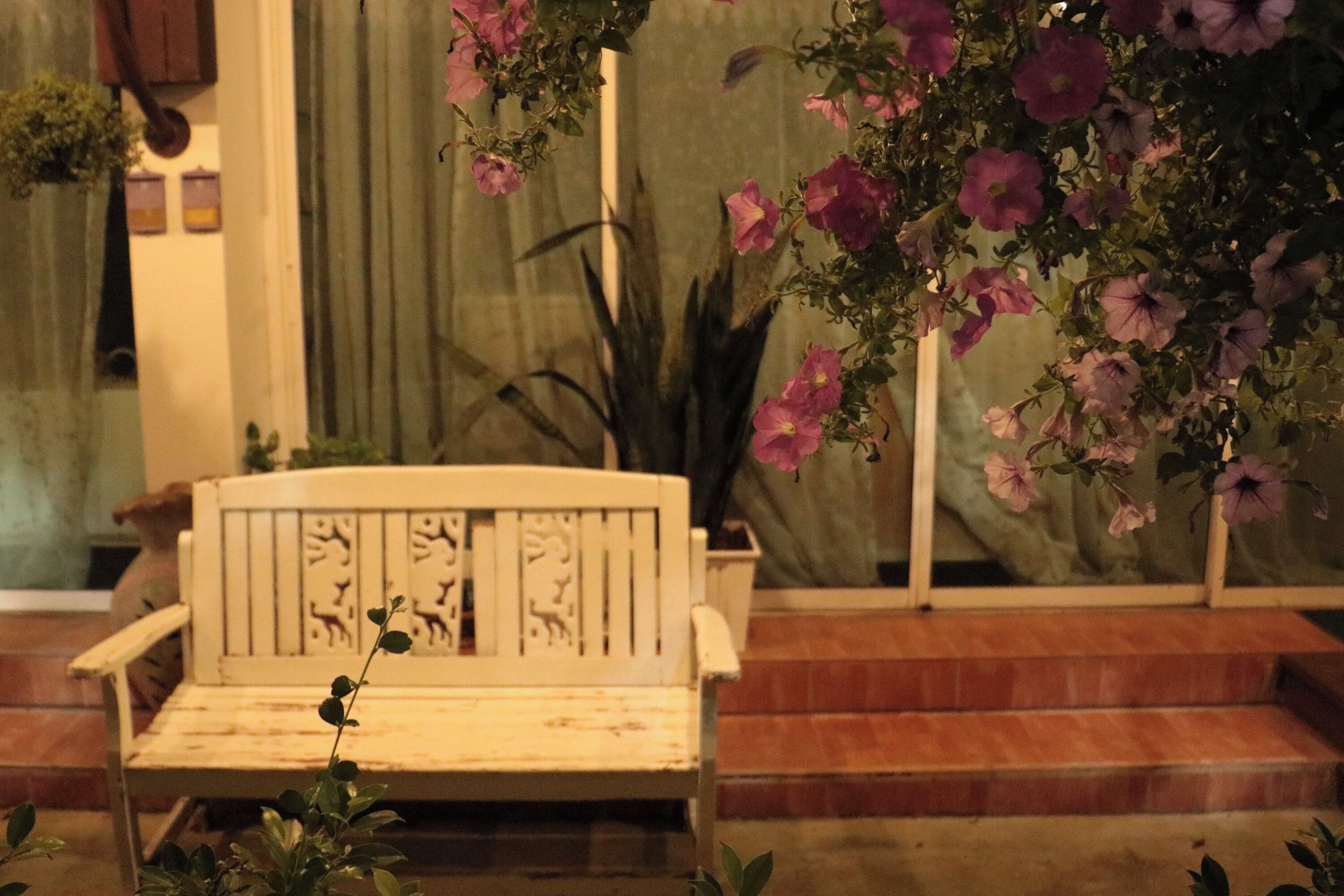 A white bench with animal carvings, surrounded by potted plants and flowers.