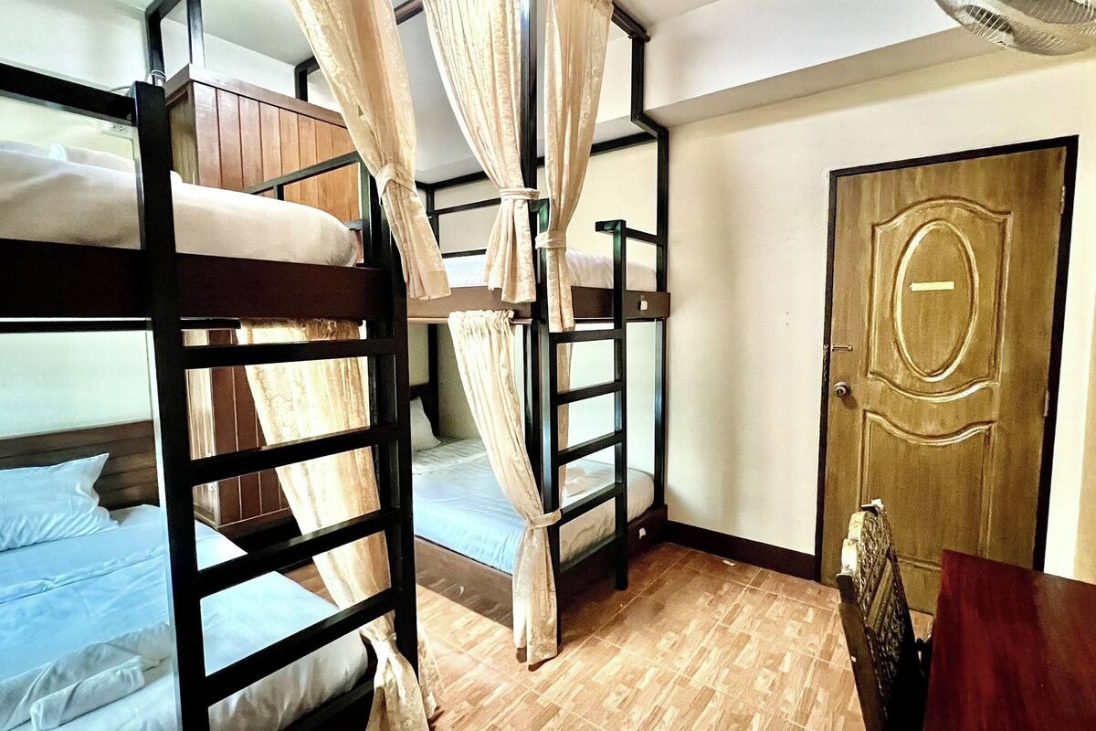 A dormitory room with bunk beds, a wooden door, and a tiled floor.