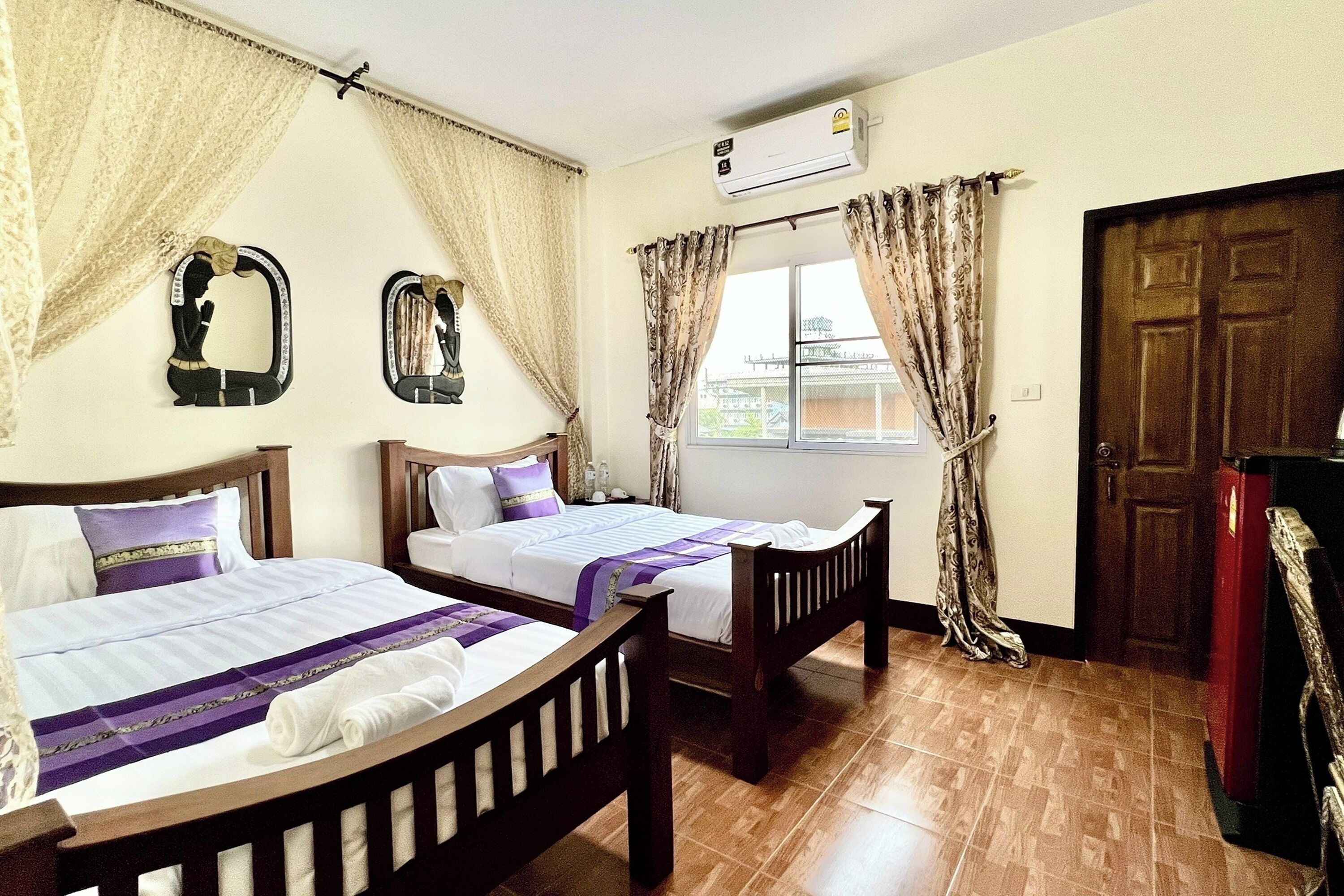 Una habitación de hotel con dos camas individuales, una ventana con cortinas, un aire acondicionado y una puerta de madera.