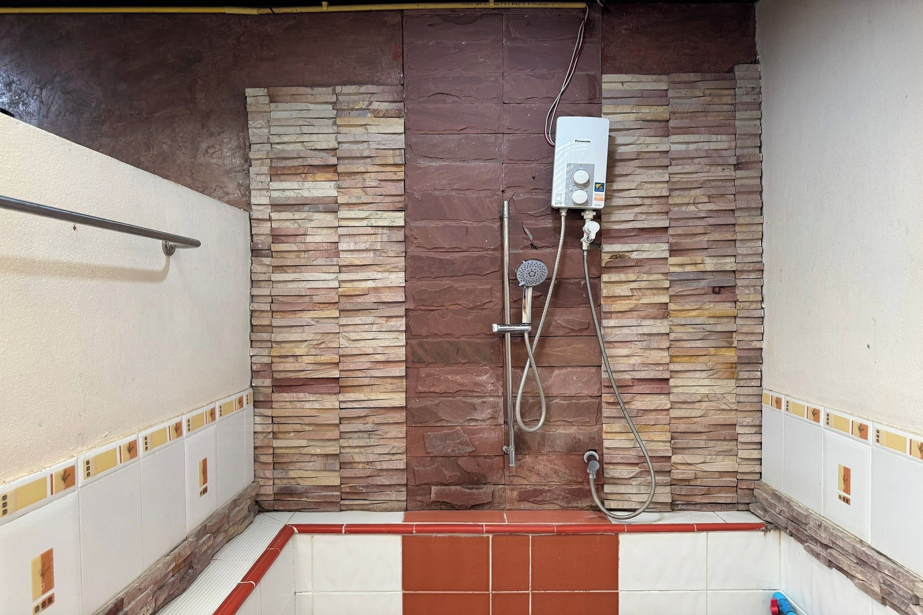 A shower area with a stone wall, a built-in water heater, and a tiled floor.