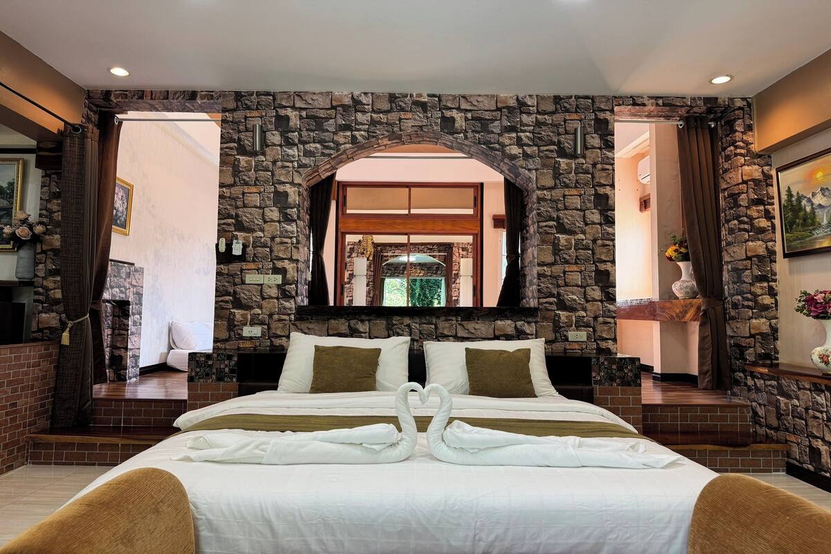 Une chambre d’hôtel avec un mur en pierre, un grand lit avec une literie blanche et une décoration en forme de cœur réalisée avec des serviettes.