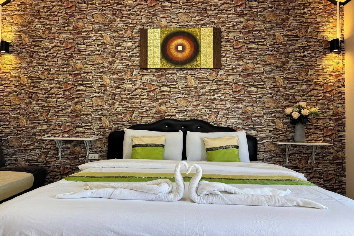 Une chambre d’hôtel avec un mur en pierre, un lit avec une literie blanche, des oreillers verts et blancs, et un tableau au-dessus du lit.