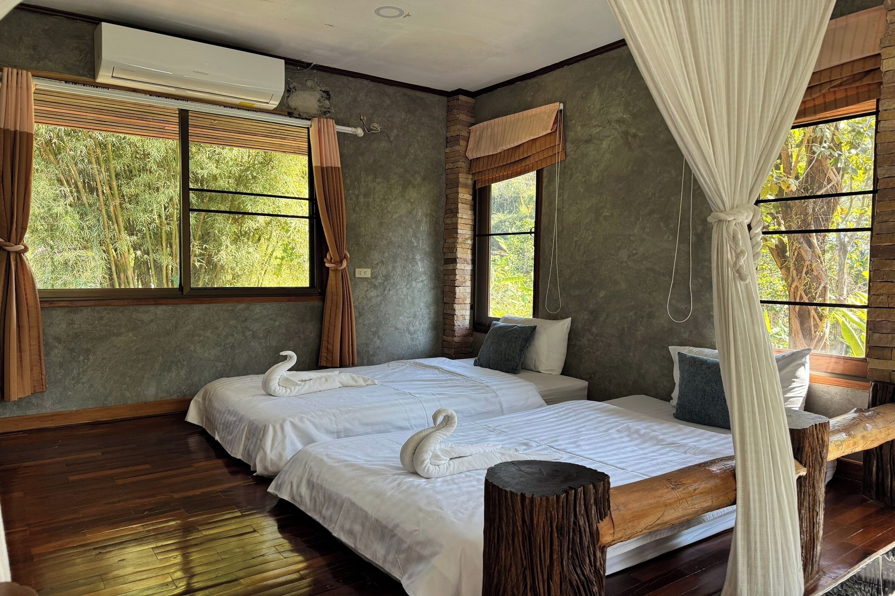 A bedroom with two beds, a wooden floor, and large windows with curtains.