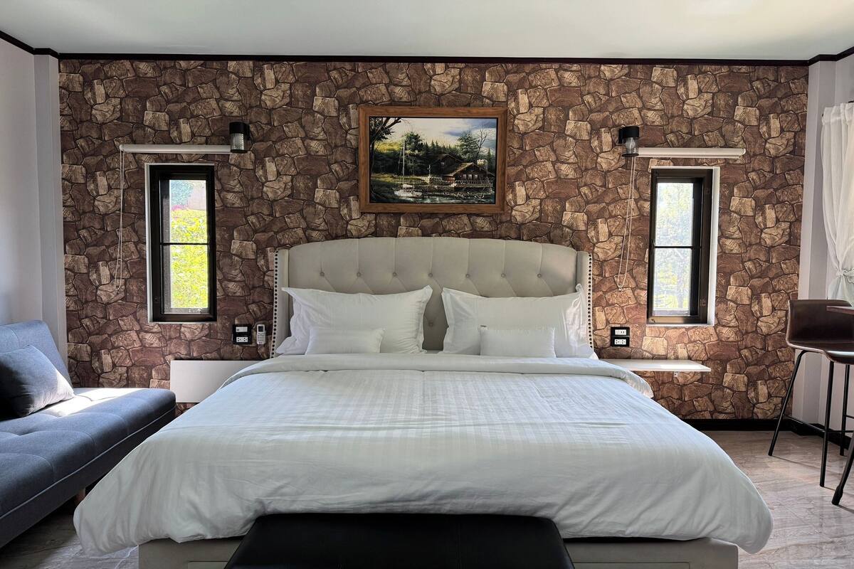 Une chambre avec un mur en pierre, un grand lit, un canapé et deux fenêtres.