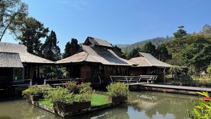 Eine traditionelle Holzhütte mit einem Reetdach, umgeben von ruhigem Wasser und üppiger Vegetation.