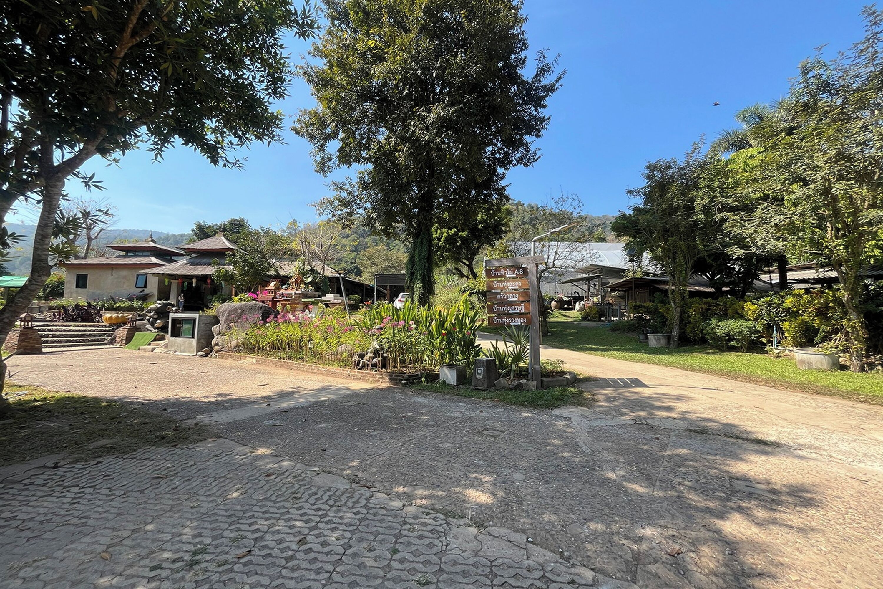 Una entrada pavimentada con un cartel señalizador, rodeada de árboles y un jardín.