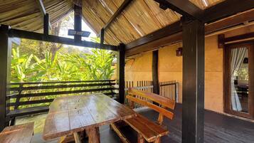 A wooden bench and table under a thatched roof, with a view of lush greenery outside.