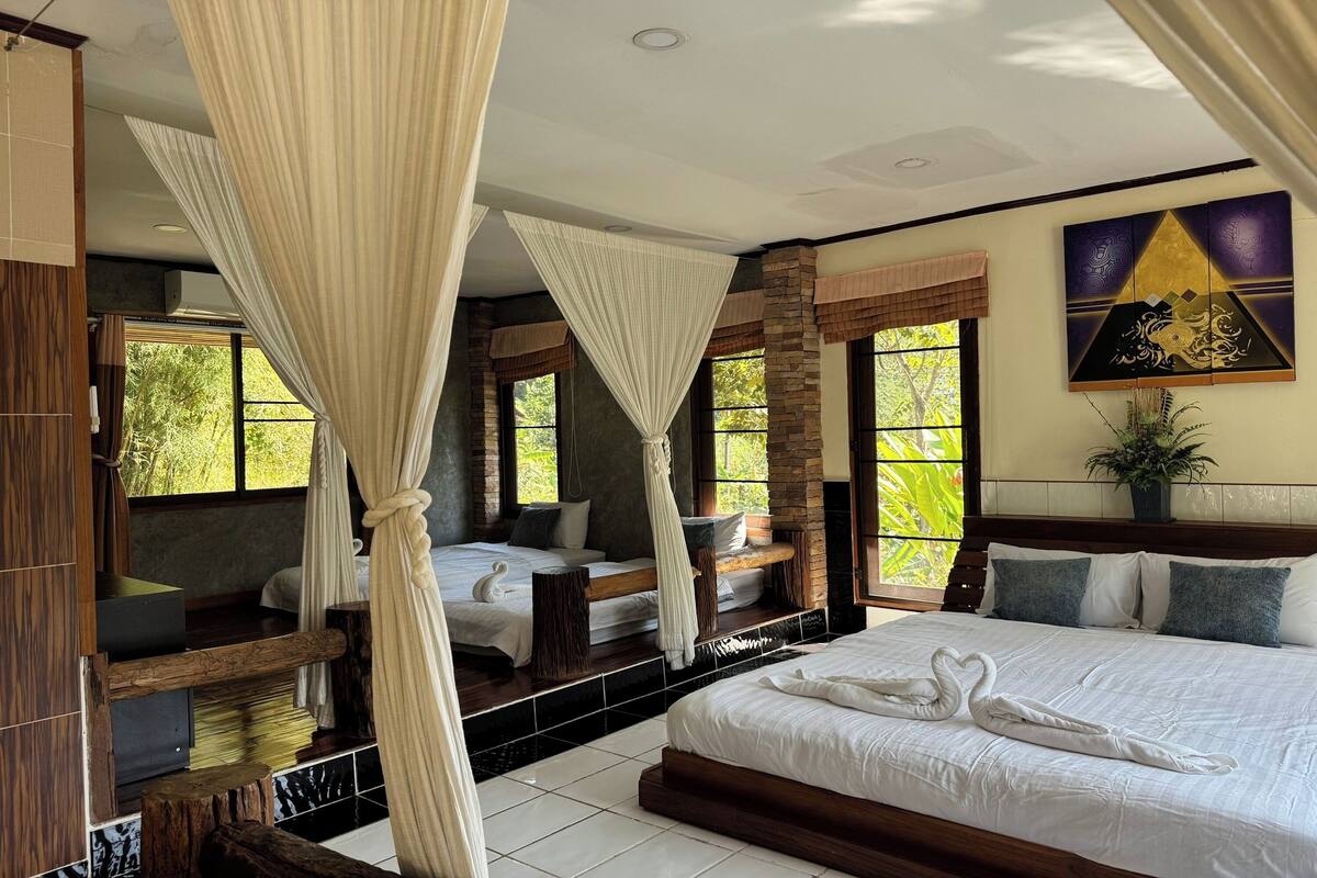 Une chambre spacieuse avec un grand lit, un lit plus petit et un coin salon offrant une vue sur la verdure.