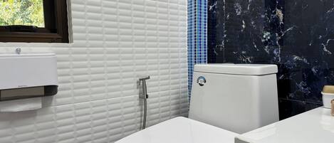 Une salle de bain avec des toilettes blanches, un lavabo blanc et une fenêtre donnant sur un paysage verdoyant.