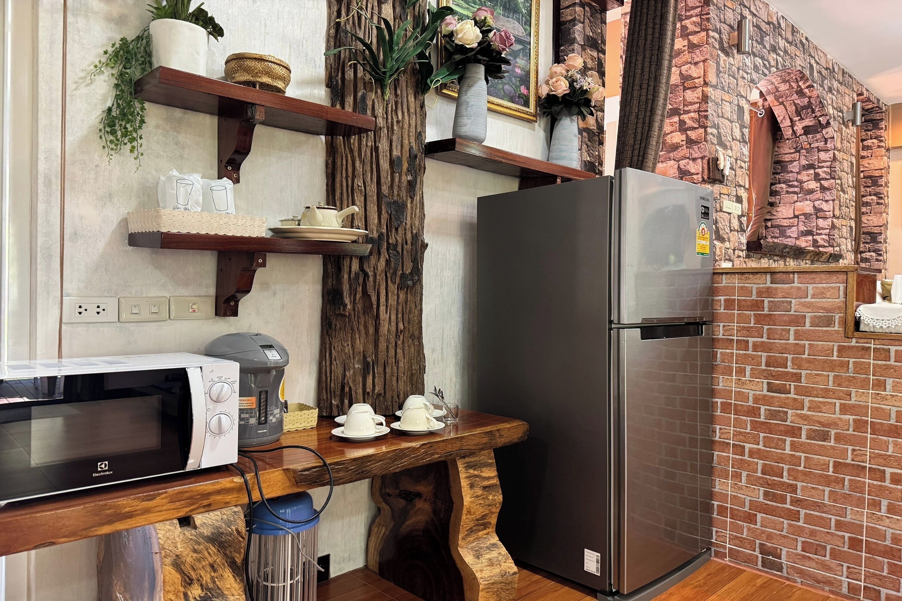 A kitchen with a built-in microwave, a refrigerator, wooden shelves with decorative items, and a rustic brick wall.