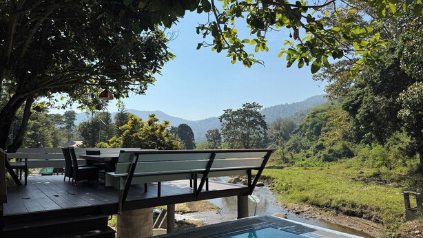 Ein Poolbereich mit Holzterrasse und Gartenmöbeln, umgeben von üppiger Vegetation und Blick auf ferne Hügel.
