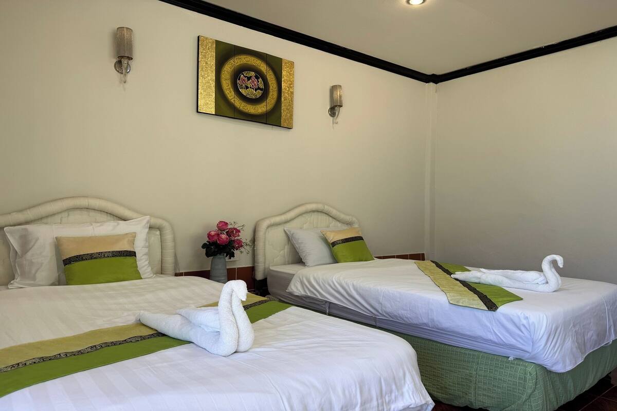 Une chambre d’hôtel avec deux lits, chacun agrémenté d’une serviette en forme de cygne, et dotée d’une literie verte et blanche, ainsi que d’un élément décoratif mural.