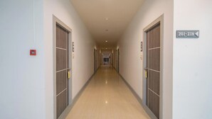 A long, narrow hotel corridor with doors numbered 201-218, a fire alarm on the left, and a sign indicating the direction to the elevators. - Top Inn Hotel (Maha Sarakham)