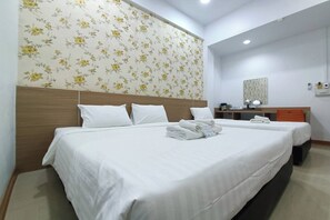 A hotel room with two beds, a wooden headboard, a floral wallpaper, a small desk with a lamp, and a mirror.