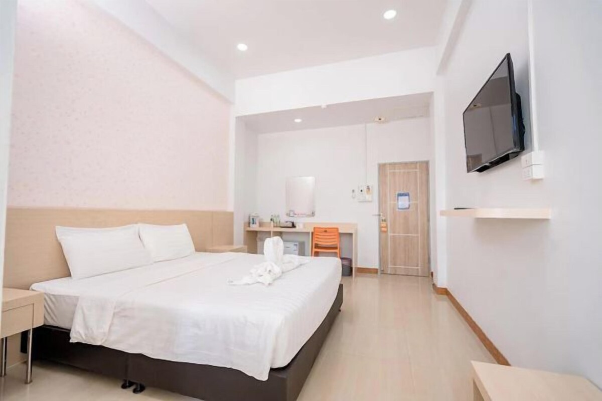 Habitació d'hotel amb llit, taula de nit, televisió i escriptori amb cadira.