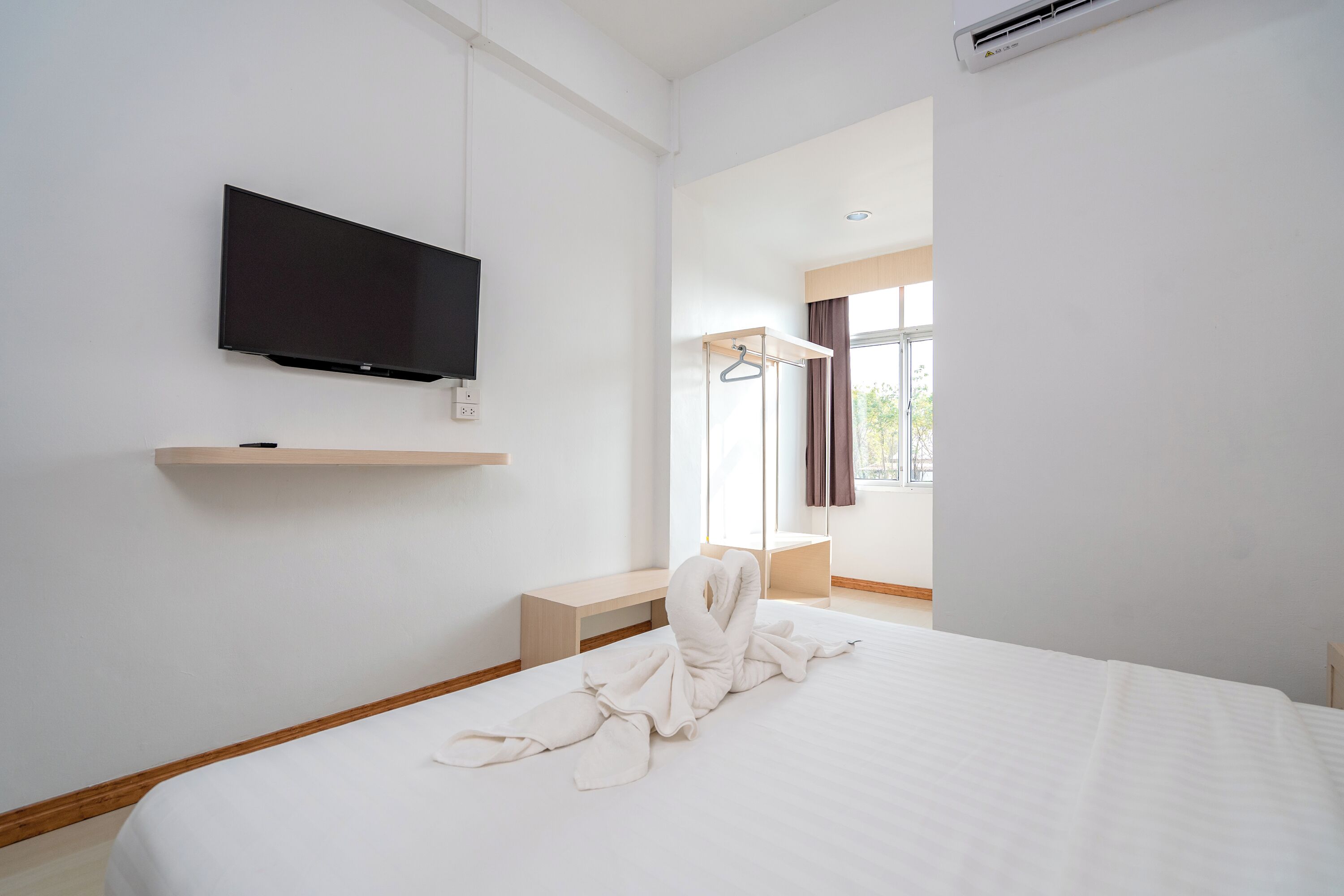 Habitación de hotel con una cama grande, un televisor de pantalla plana en la pared, un banco de madera y una ventana con cortinas.