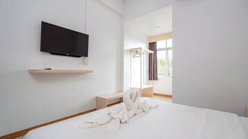 Habitación de hotel con una cama grande, un televisor de pantalla plana en la pared, un banco de madera y una ventana con cortinas.