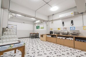 A cafeteria with a buffet setup, including glassware, plates, and a coffee machine.