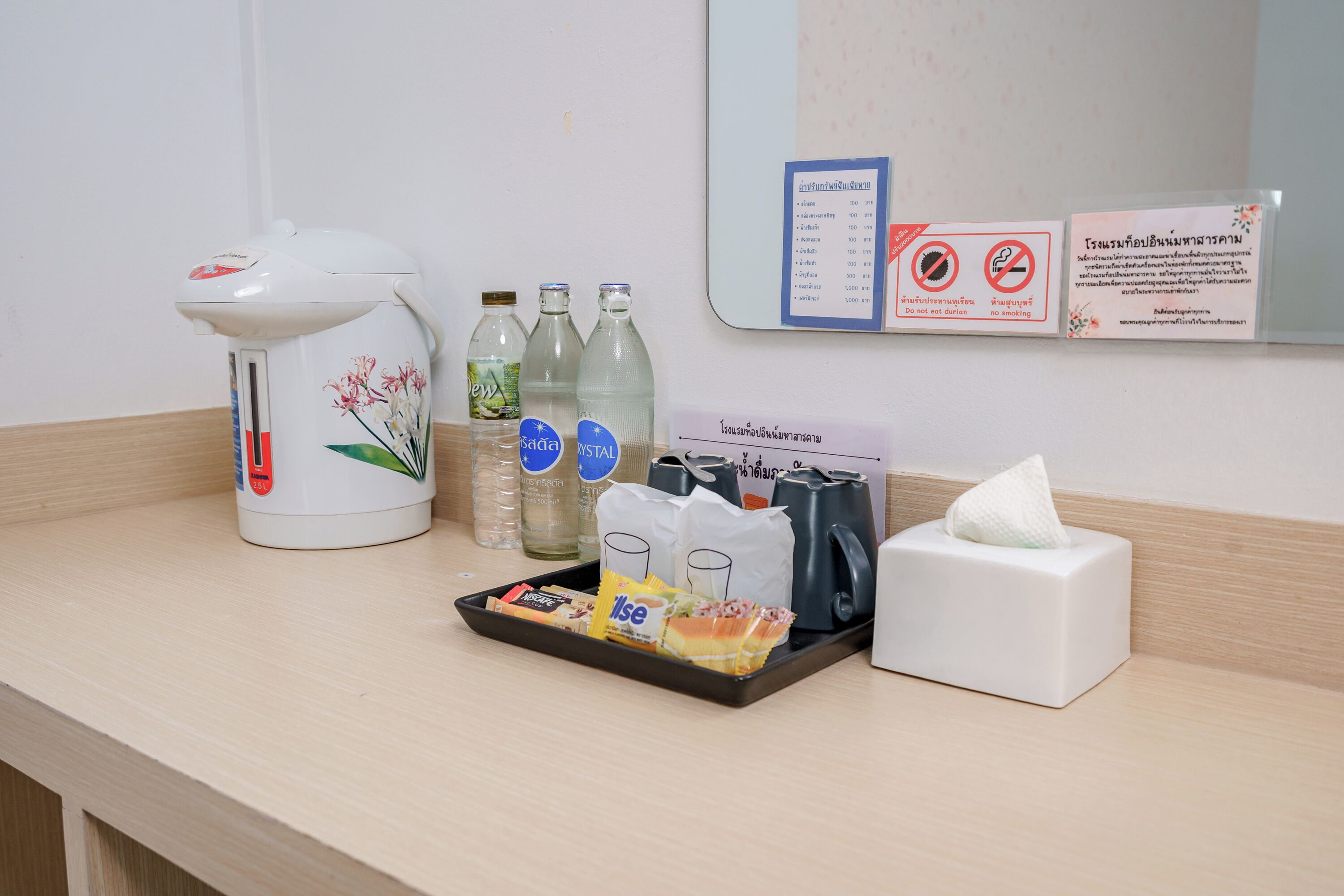 A hotel room counter with a coffee maker, bottled water, a tray with snacks, and a tissue box.