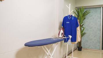 A room with a blue ironing board, an iron, and a hanging blue shirt.