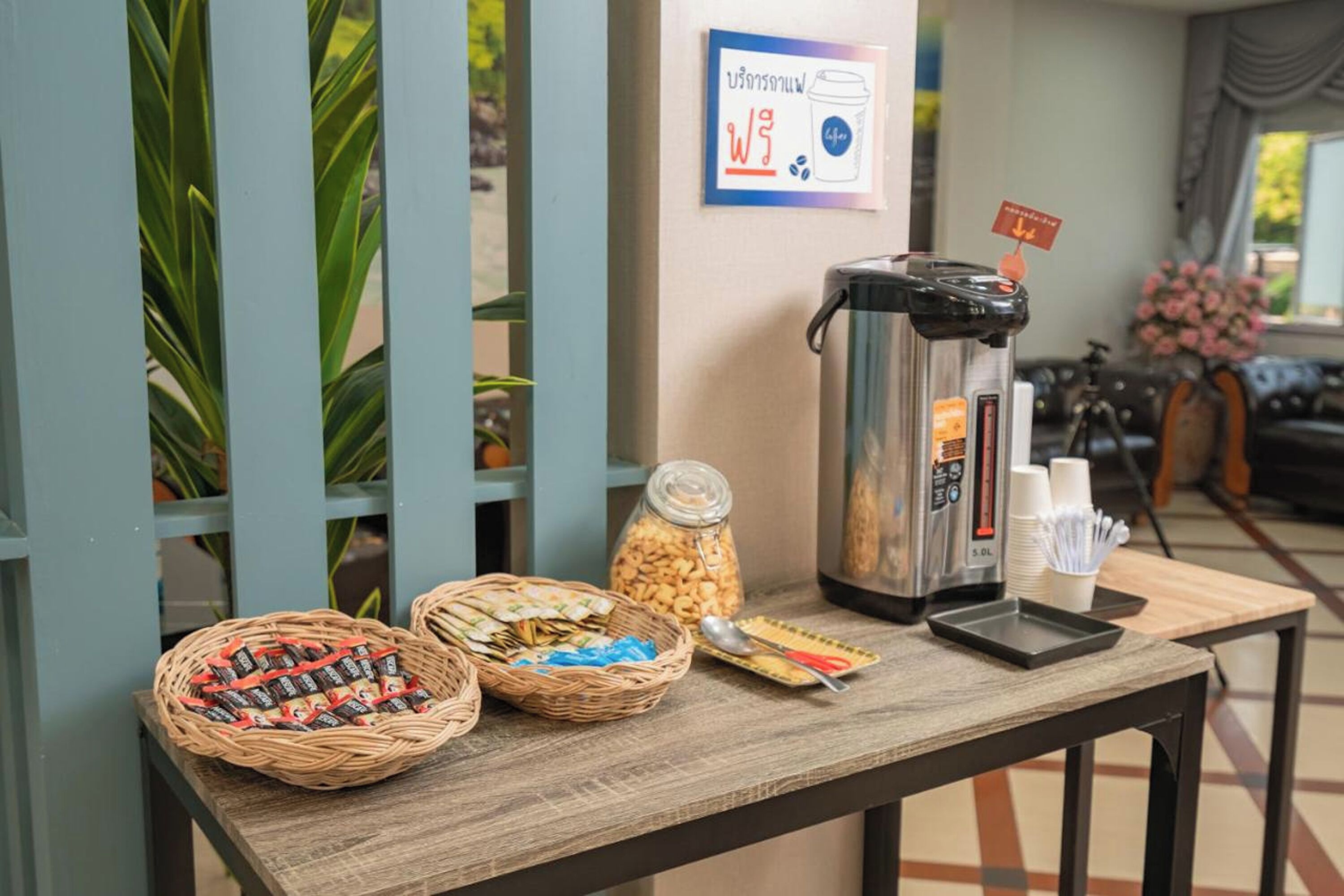 Una mesa de desayuno con una cafetera, cestas de aperitivos y un letrero que indica una estación de café.