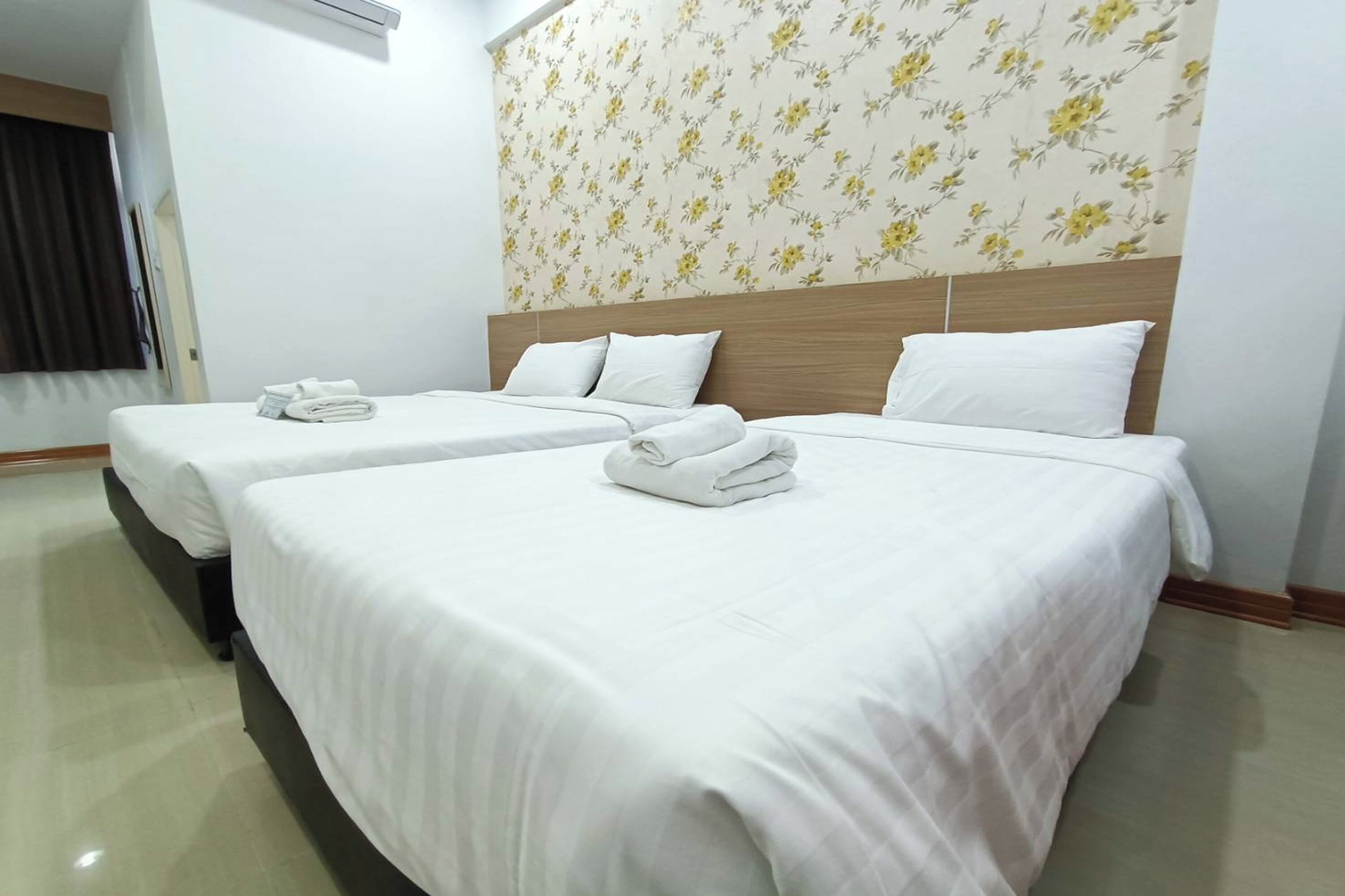 Ett hotellrum med två sängar, båda med vita lakan och handdukar, ett träfärgat sänggavel och en tapet med blommönster.