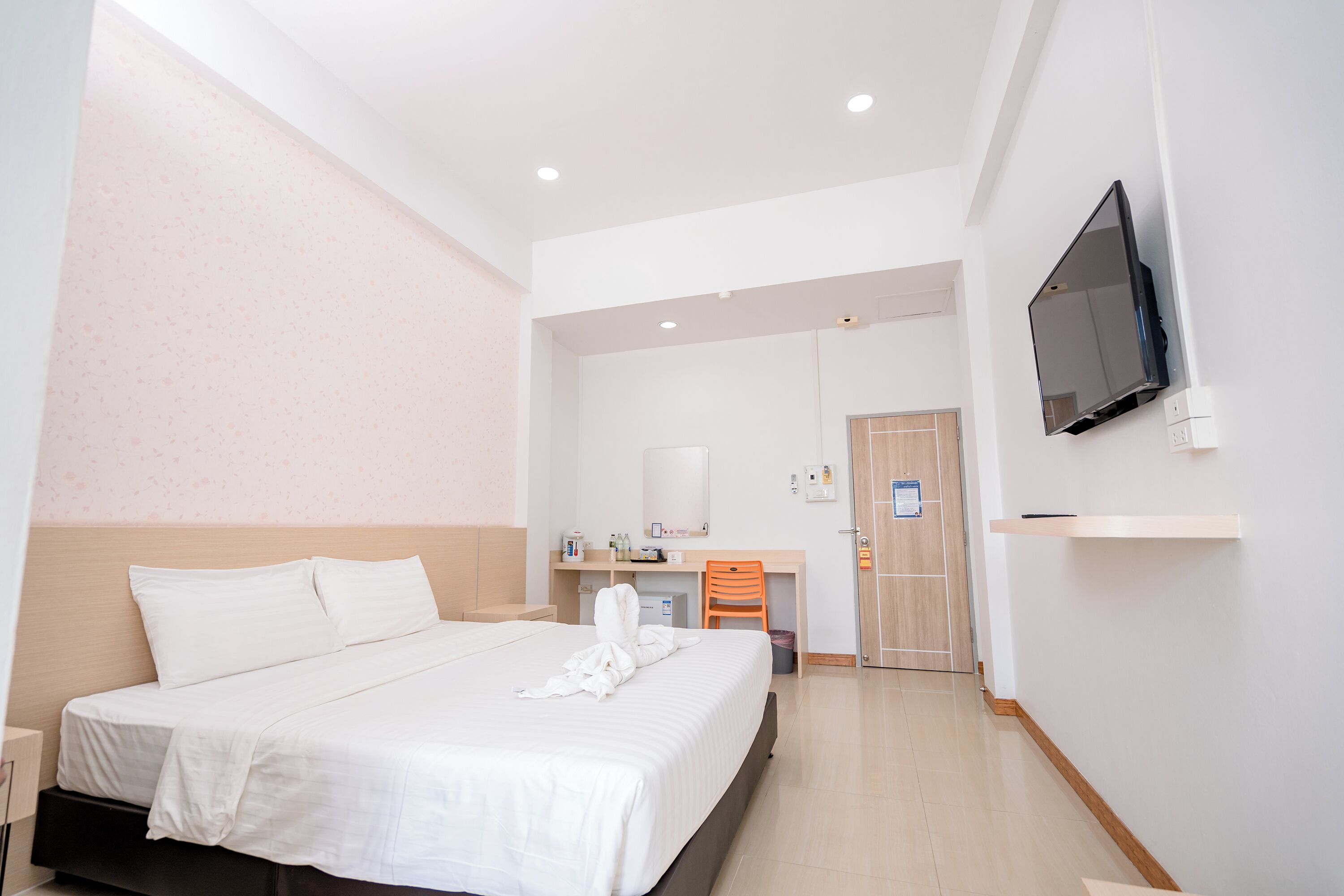 A hotel room with a bed, a desk, a chair, a television, and a door.