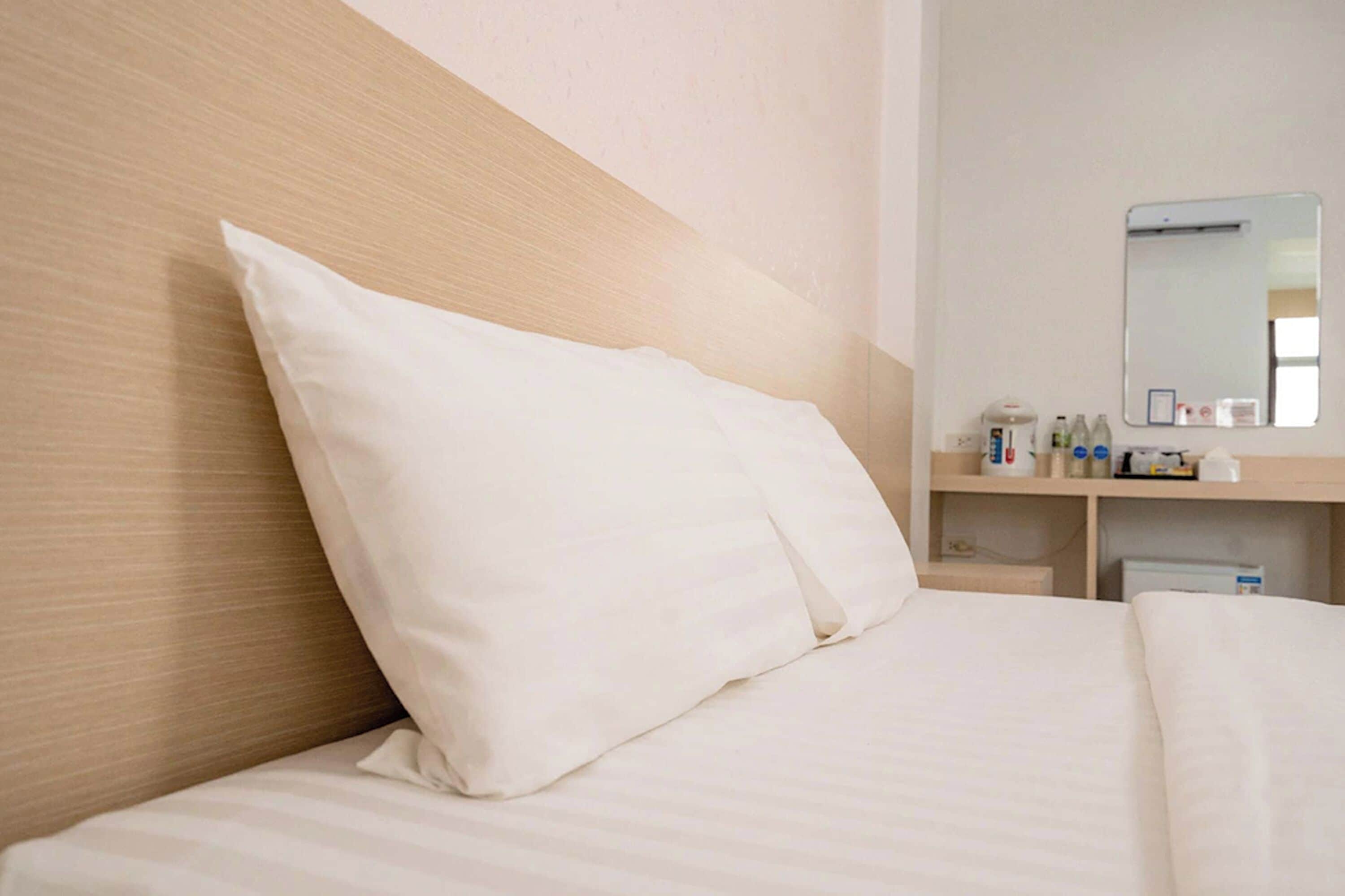 A hotel room with a bed, a wooden headboard, a bedside table with toiletries, and a mirror.
