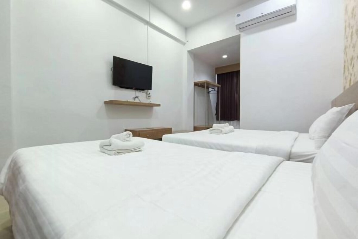 A hotel room with two beds, a flat-screen TV mounted on the wall, a mirror, and an air conditioning unit.