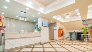 A hotel lobby with a reception desk, a large open space with patterned flooring, and a staircase leading to an upper level. - Top Inn Hotel (Maha Sarakham)