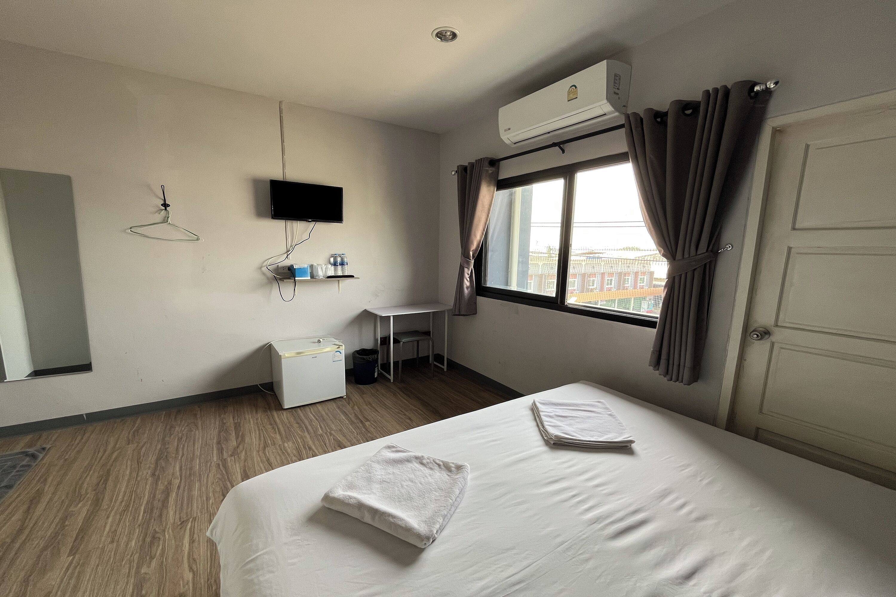 A hotel room with a bed, a desk, a chair, a TV, and an air conditioning unit.