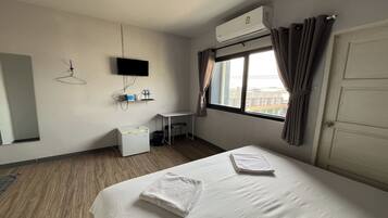 A hotel room with a bed, a desk, a chair, a TV, and an air conditioning unit.