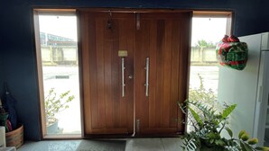 A wooden door with a push bar, a potted plant, and a wall-mounted item. - Blue 26 (Sam Phran)