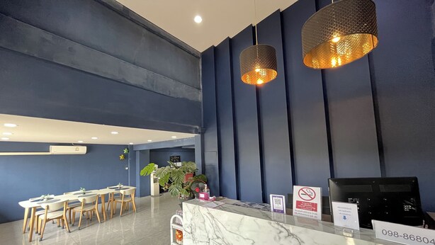 A hotel reception area with a marble counter, two pendant lights, a reception desk, and a seating area with tables and chairs. - Blue 26 (Sam Phran)