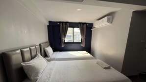 A hotel room with two beds, a window with curtains, an air conditioning unit, and a view of the outside. - Blue 26 (Sam Phran)