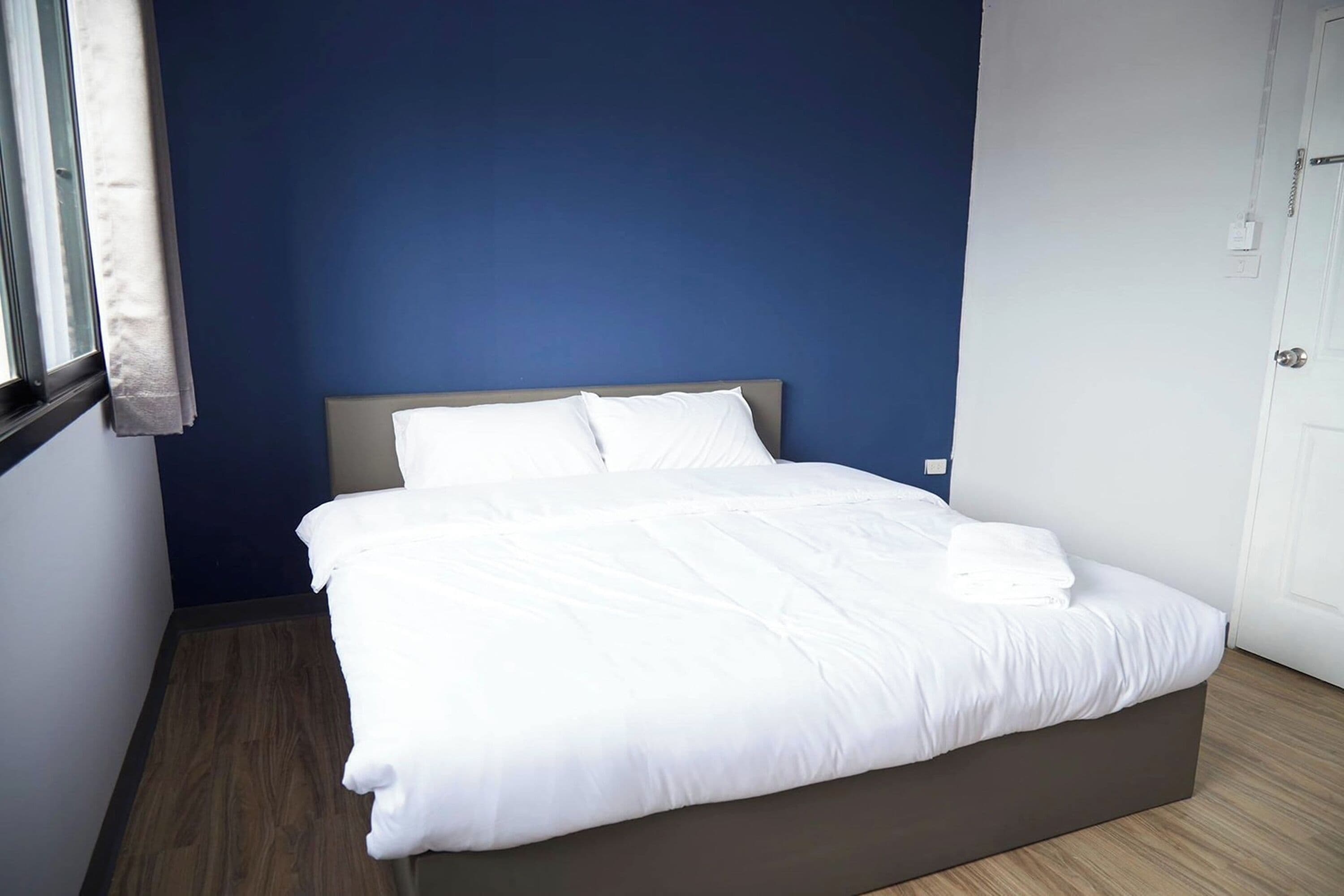 A neatly made bed with white linens in a room with blue walls and a wooden floor.