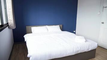 A neatly made bed with white linens in a room with blue walls and a wooden floor.
