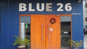 A building with a blue exterior and a wooden double door. - Blue 26 (Sam Phran)