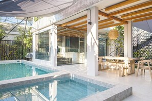 A modern outdoor pool area with a glass enclosure, wooden deck, and seating.