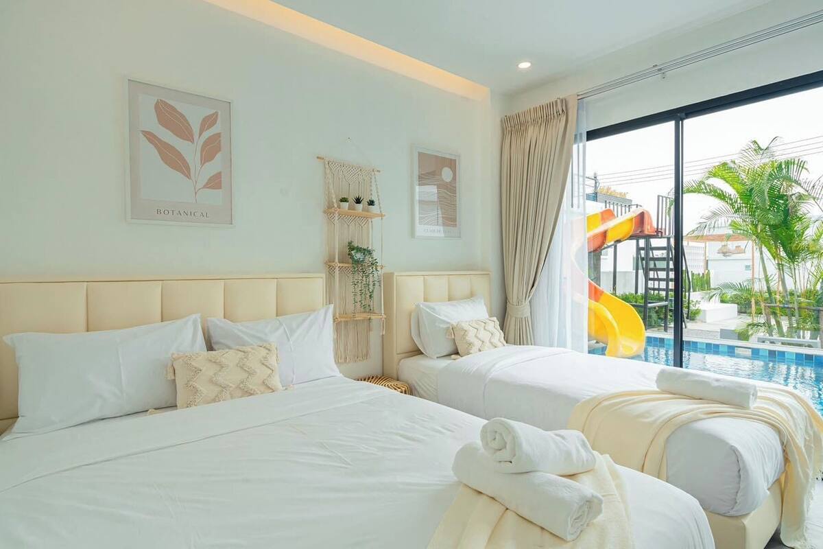 Une chambre d’hôtel avec deux lits, une décoration murale en macramé et une vue sur une piscine avec un toboggan.