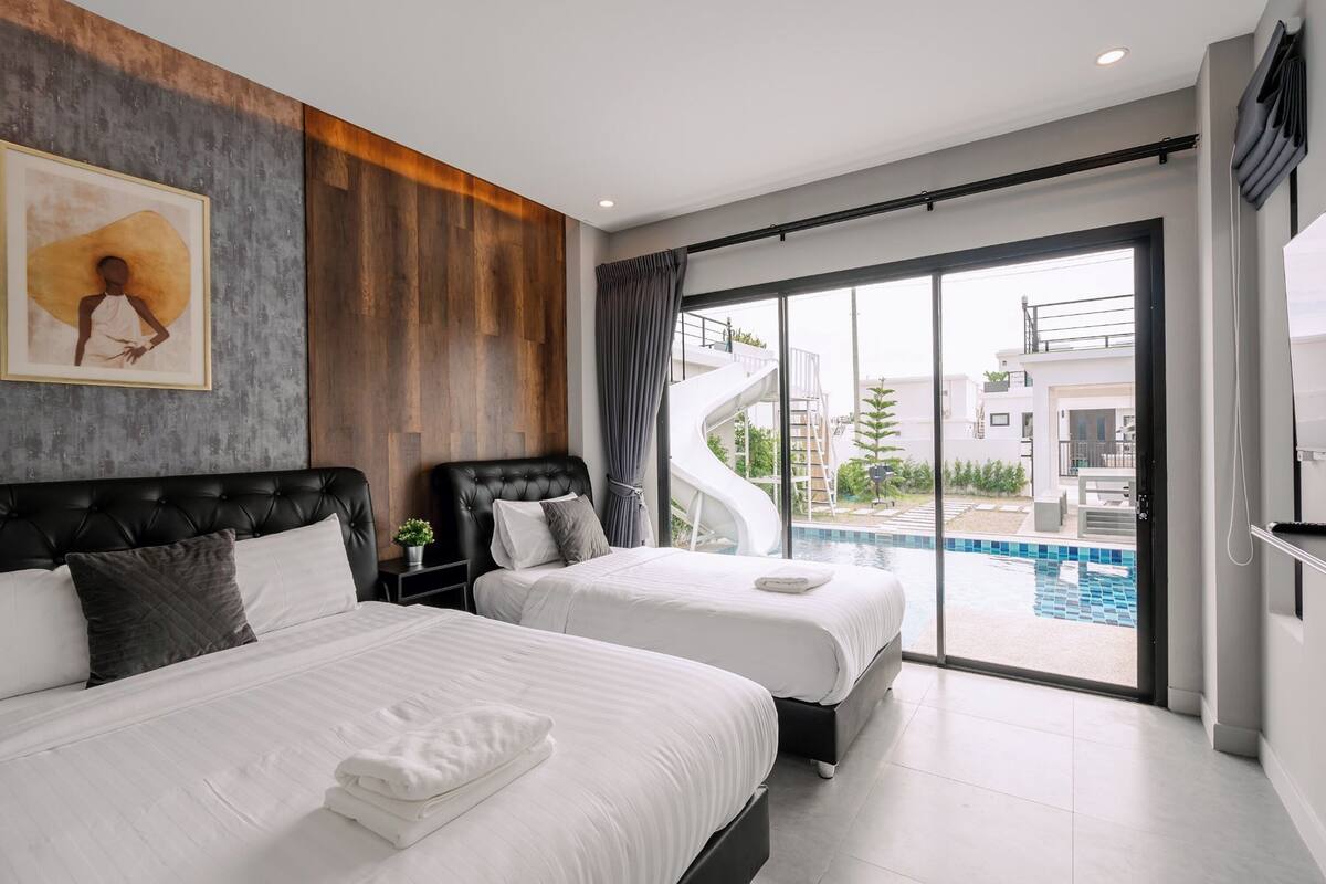 Une chambre d’hôtel moderne avec deux lits, une grande fenêtre donnant sur une piscine et un escalier en colimaçon.