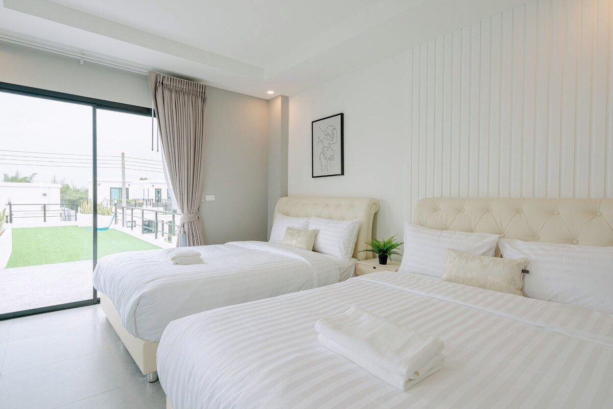 Een hotelkamer met twee bedden, een groot raam, een schuifdeur naar een buitenruimte en een ingelijst schilderij aan de muur.