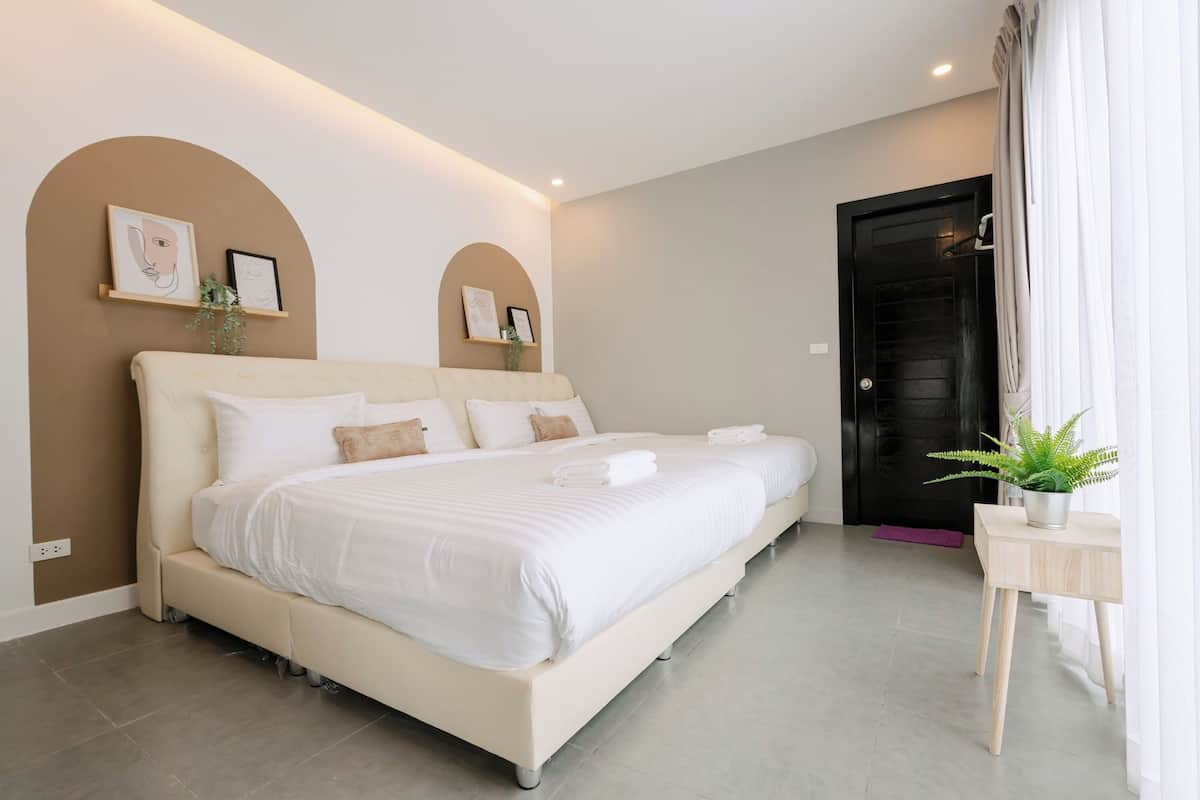Une chambre d’hôtel moderne avec un grand lit, une petite table de chevet agrémentée d’une plante et une porte avec des rideaux.