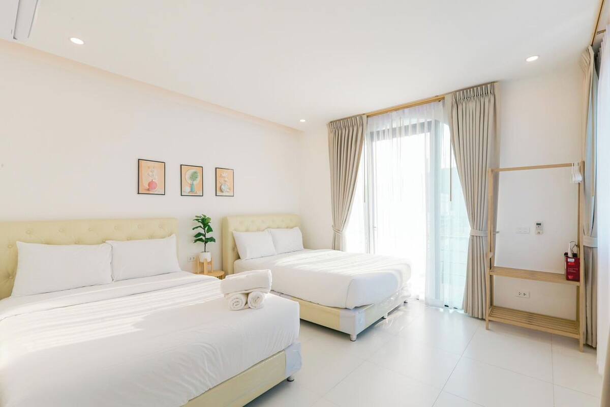 Une chambre d’hôtel avec deux lits, une table de chevet avec une lampe, une fenêtre avec des rideaux et une petite étagère avec une bouteille.