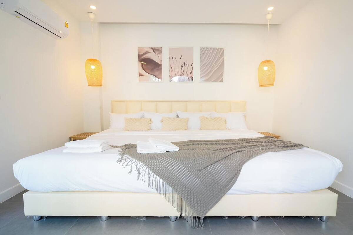 Une chambre moderne avec un grand lit, une literie blanche, un plaid gris et deux lampes fixées au mur.