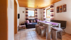 Una habitación acogedora con techo de madera, un sofá, una mesa de comedor con taburetes y cortinas a rayas.